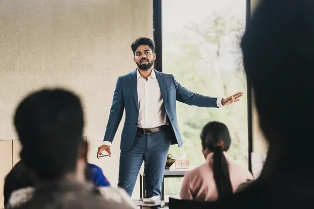 The speaker with both arms open, addressing founders seated at the front
