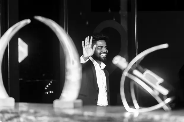 Black and white frame of the speaker with a hand raised, mid-sentence